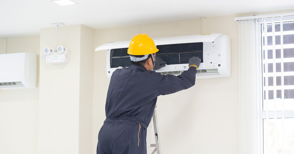 A man in a hard yellow hat inspects an air conditioning unit