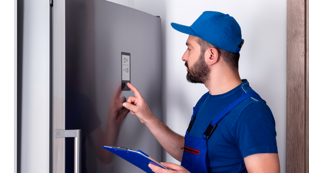 Worker in blue uniform and cap whilst holding a clipboard adjusts a refrigerator touchscreen panel.