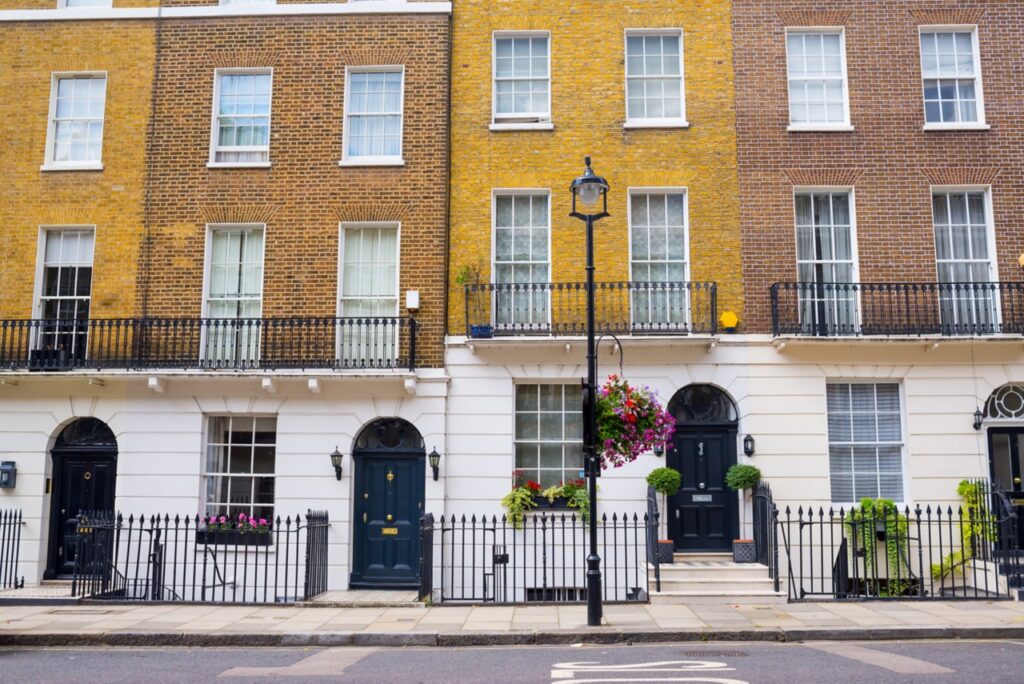 Elegant row of brick townhouses with black railings, arched doorways, hanging flower baskets and large windows.