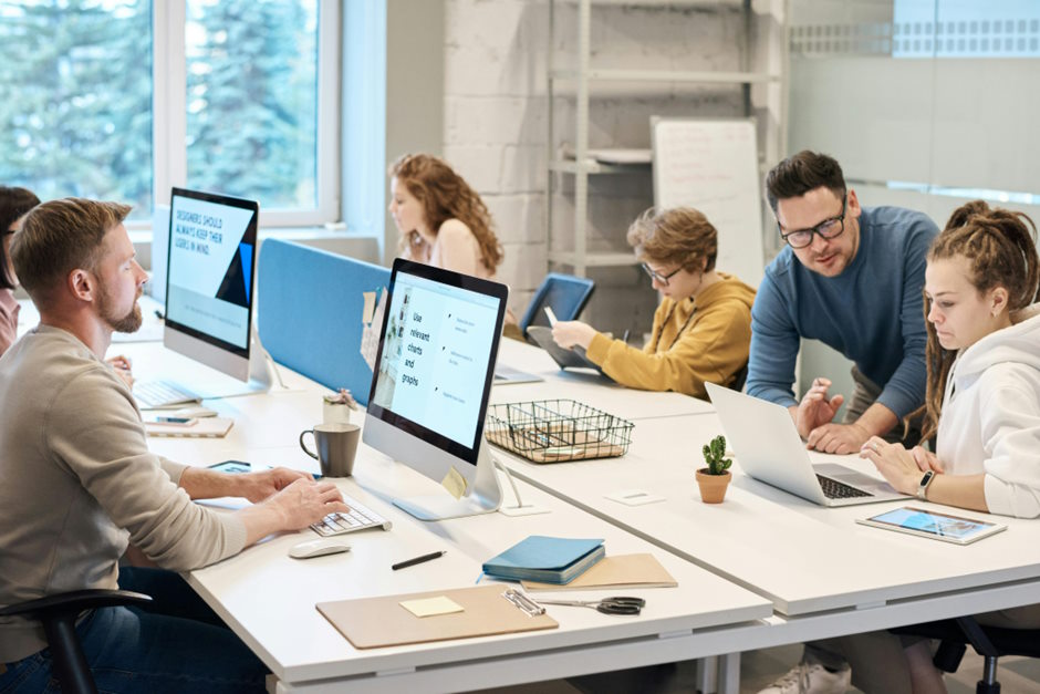 A group of people using computers and laptops working together in a modern, bright office.